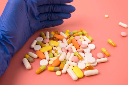 Close up of doctor hand in blue glove and many different pills on pink background.の写真素材