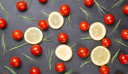 Red cherry tomatoes, orange and lemon slices and green salad leaves on dark black background.の写真素材