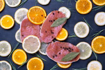 Raw meat stakes, orange and lemon slices and green salad leaves on dark black background.の写真素材