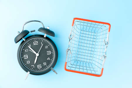 Black vintage analog alarm clock and small shopping basket on blue background.の写真素材