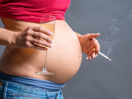 Concept of unhealthy habits during pregnancy. A pregnant woman smoking cigarette and drinking Alcohol and coffee.の写真素材