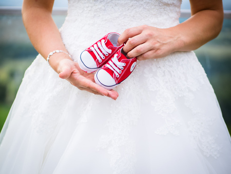 The pregnant bride has the little baby shoes in front of her stomachの写真素材
