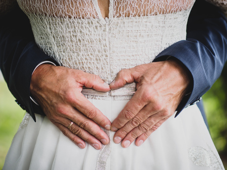 Groom creating heart shape with his hands on the back of the bride.Couple in love. Close up of hands. Young couple has done heart shape hands in their wedding day. Bride and groom, embrace.の写真素材