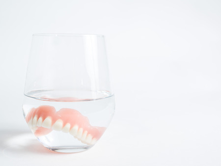 The one acrylic dentures immersed in a glass of water white backgroundの写真素材