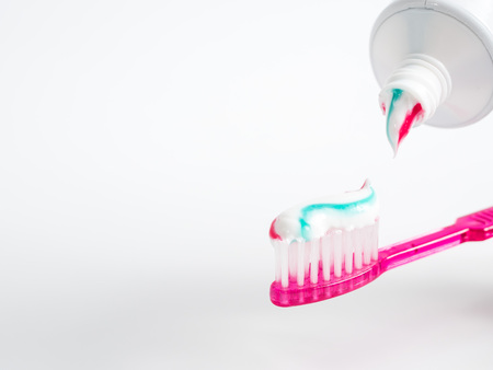 The red blue striped toothpaste is applied to a toothbrush on a white backgroundの写真素材