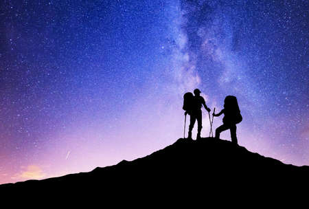 Silhouettes of team on mountain peak. Sport and active life concept on the night sky backgroundの写真素材