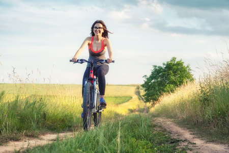 Girl ride on a bike ion the field at the summer time Sport and fitness concept