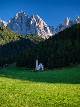 Santa Maddalena. Val di Funes. Dolomite Alps. Italy. Church in the meadow. The mountains and the forest before sunset. Natural landscape in the summertime. Photo in high resolution.の写真素材