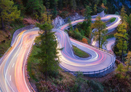 The mountain pass of Maloja, Switzerland. A road with many curves among the forest. A blur of car lights. Landscape in evening time. Large resolution photo for design.の写真素材