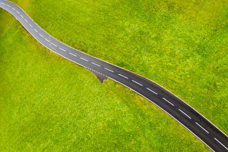 A straight road in a green meadow. Asphalt and grass. An aerial landscape from a drone as a backdrop. Swiss landscapeの写真素材