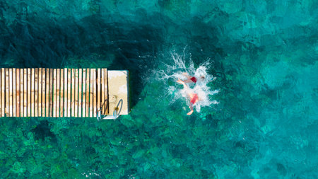 A carefree couple jumps into the azure sea. Aerial view. A vacation in the summertime. Young and energetic people dive into the water together. A fun vacation at the sea together.の写真素材
