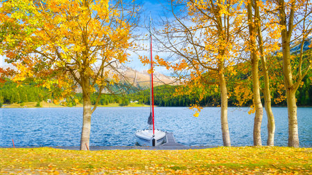 Autumn landscape on the lakeside. Trees with yellow leaves. A boat on the shore of a mountain lake. Natural landscape in autumn time.  Holiday spot.の写真素材