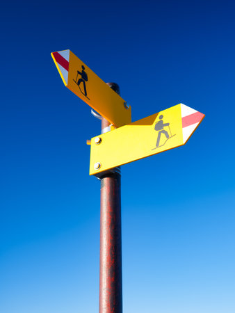 Directional marker for a mountain hike. Yellow bright sign with an arrow against the blue sky. Navigation in a hiking trip.の写真素材