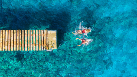 A carefree couple jumps into the azure sea. Aerial view. A vacation in the summertime. Young and energetic people dive into the water together. A fun vacation at the sea together.の写真素材
