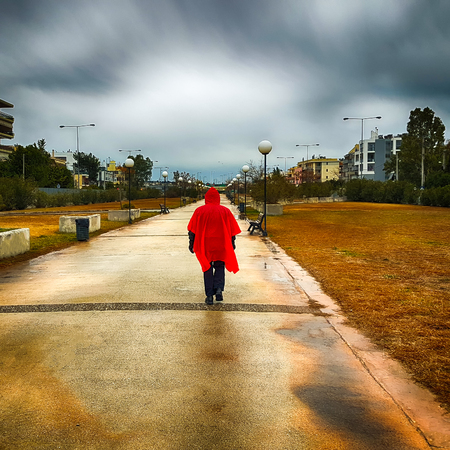Stranger with a red coat walking at a park on a rainy day against a dramatic sky.の写真素材
