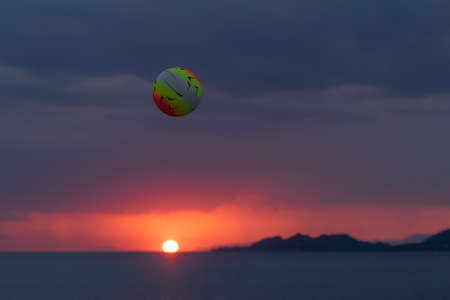 Beach volley ball up in the air while playing against a vivid sunset.