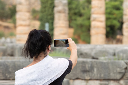 Woman taking a photo at the sanctuary of Apollo at Delphi in Greece. A famous touristic destination.