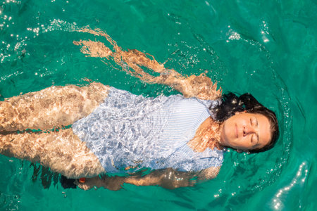 Beautiful woman wearing blue white swimsuit relaxing in the sea enjoying summer in Zakynthos island in Greece.の写真素材