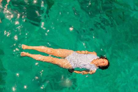 Beautiful woman wearing blue white swimsuit relaxing in the sea enjoying summer in Zakynthos island...