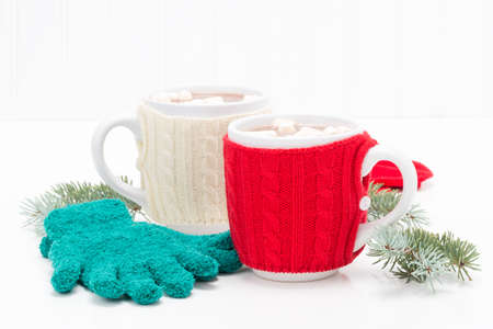 Two mugs of creamy hot chocolate with gloves and spruce.の写真素材