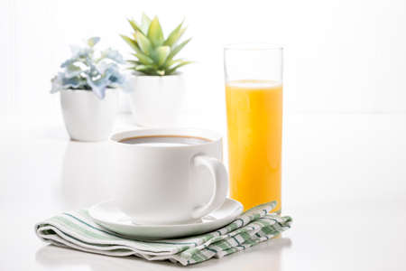 Cup of hot coffee and glass of orange juice with potted plants in background.の写真素材