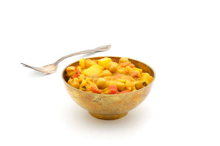 Indian chickpea and potato curry in a vintage brass bowl on a white background.の写真素材