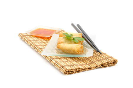 Plate of vegetarian Thai spring rolls served with a spicy dipping sauce on a white background.