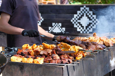 Man in black T-shirt roasts a barbecue on grill. Street food and outdoor cooking concept.の写真素材