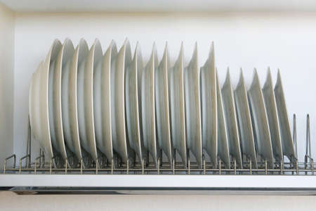 Shelf for tableware drying in modern kitchen. White glass and ceramic dishes on metal rack inside...