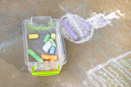 Crayons of blue, green, yellow, white in plastic box. Painted with colored crayons floor tiles in...