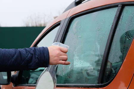 Man cleaning his orange automobile with spray. Washing automobile window. Drops on glass.の写真素材
