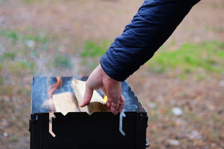 Lighting the grill. Man kindles fire for grilling. Man's hand is adding wood into fire.
