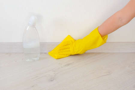 Employee hand in yellow rubber protective glove with micro fiber cloth wipes the floor and plinth....
