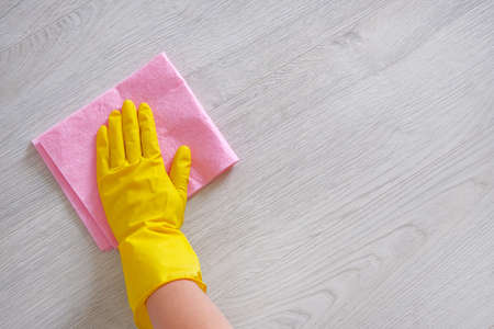 Cleaning concept in office, home. Female hand with pink rag is wipes light wooden floor at home....