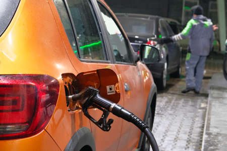 Car fill with diesel at petrol station. Pumping diesel fuel in orange car at gas station in evening.