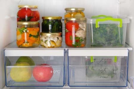 Variety glass jars homemade pickled vegetables and other products stand in fridge. Fermented healthy natural vegetarian food concept.の写真素材