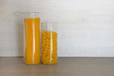 Pasta in large glass jars containers stand on gray table in kitchen. Uncooked raw italian pasta with spaghetti.の写真素材