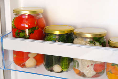 Jars of various homemade pickled vegetables on shelf of refrigerator. Fermented healthy natural vegetarian food concept.の写真素材