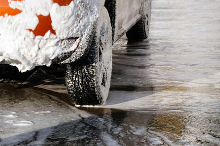 Car is cleaning with soap suds at self-service car wash. White soap suds on auto. Car wheel close...