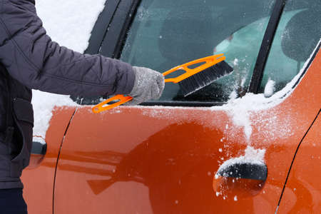 Car covered with snow. Man brushing and shoveling snow off car after snow storm. Brush in mans hand.の写真素材
