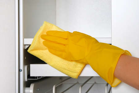 Housewife wearing protective gloves is doing housework. Hand in yellow protective glove is wiping white furniture with rag.の写真素材