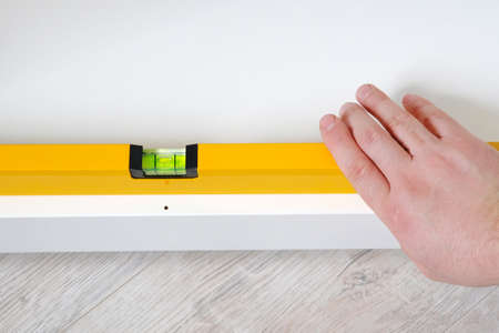 Repairs in house or apartment. Male hand repairing white furniture with level in house or apartment,...