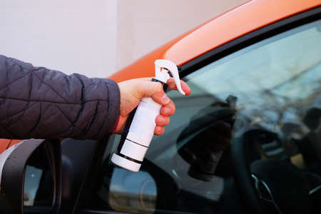 Man after washing uses anti-rain spray for car glass windows. Male hand and car body close up....