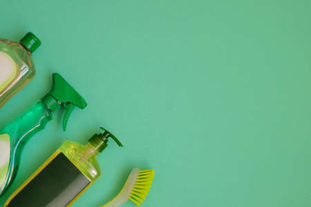 Cleaning products on green background. Detergents in plastic bottles and brush. Housekeeping chores. Top view. Copy space.の写真素材