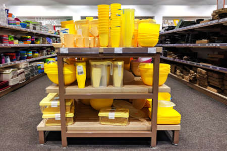 Plastic yellow cookware are sold at the shop. Rows of different kitchen utensils for home on shelves...
