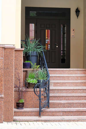 Pots of flowers and plants stand on the steps at the entrance to the house. Residential porch...