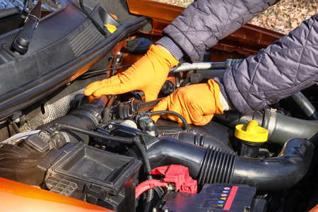 Auto maintenance concept. Hands of driver in orange rubber gloves checks car, open hood. Cars and...