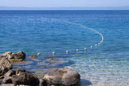 Rope with white buoys above the surface of the blue water. Bounding buoys at sea. Horizontal view....
