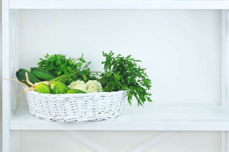 Green autumn vegetables in basket on shelf in wooden rack near a white wall. Copy space for putting text.の写真素材