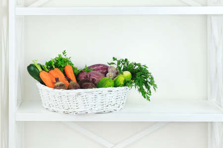 Autumn vegetables in basket on shelf in wooden rack near a white wall. Empty space for putting text.の写真素材